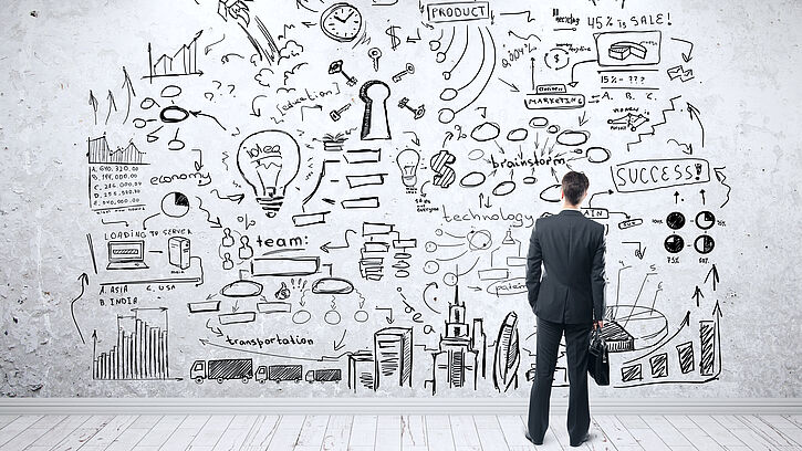 Person in Business-Kleidung steht vor einer Wand, auf der verschiedene Symbole und Icons im Zusammenhang mit Business-Strategie