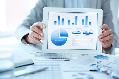 Auf dem Bild hält eine Person ein Tablet mit verschiedenen Auswertungen in die Kamera