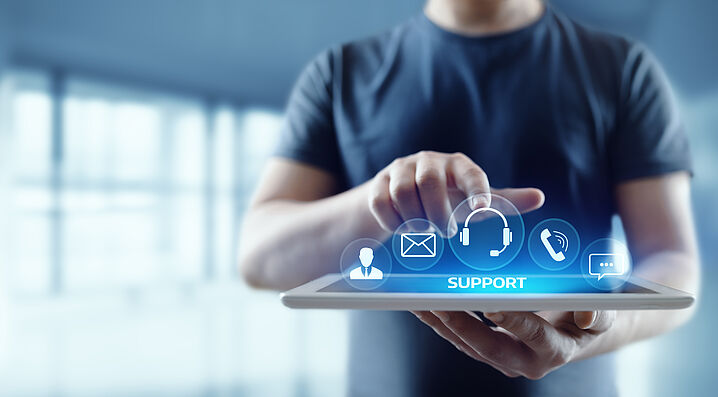 In the image, a person is holding a tablet, above which float the word “Support” and icons related to customer service.