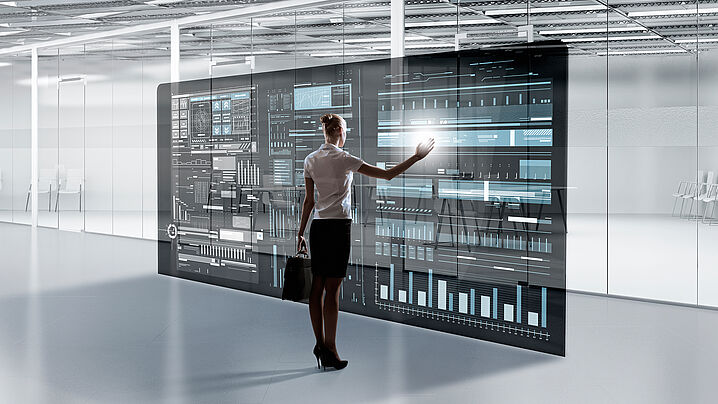 Abbildung zeigt eine Person, die vor einem großen Bildschirm mit einem User Interface steht