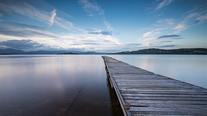 Foto eines Stegs, der über einen See hinweg in die Ferne führt