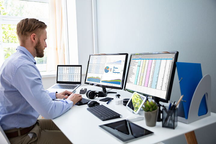 A person is sitting in front of two screens and a laptop displaying analyses.
