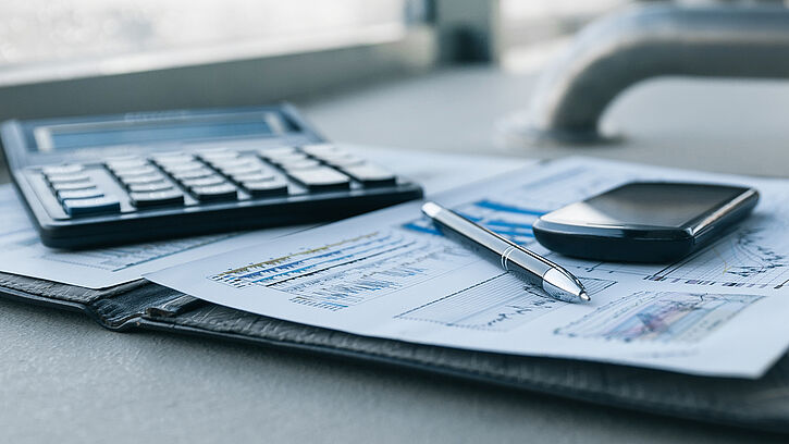 Taschenrechner, Kugelschreiber und Smartphone liegen auf ausgedruckten Dokumenten mit Statistiken