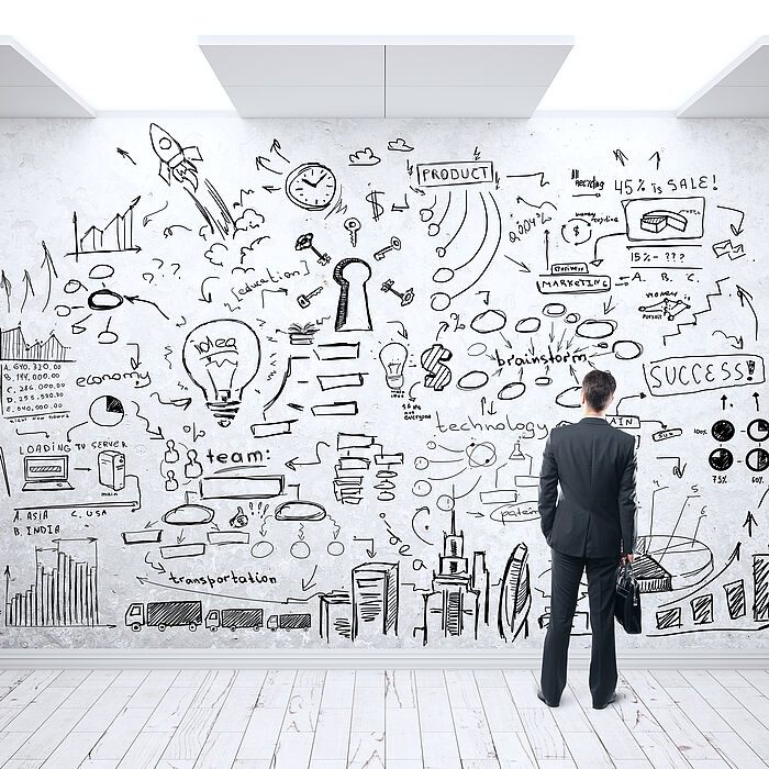 Person in business attire standing in front of a wall displaying various symbols and icons related to business strategy.